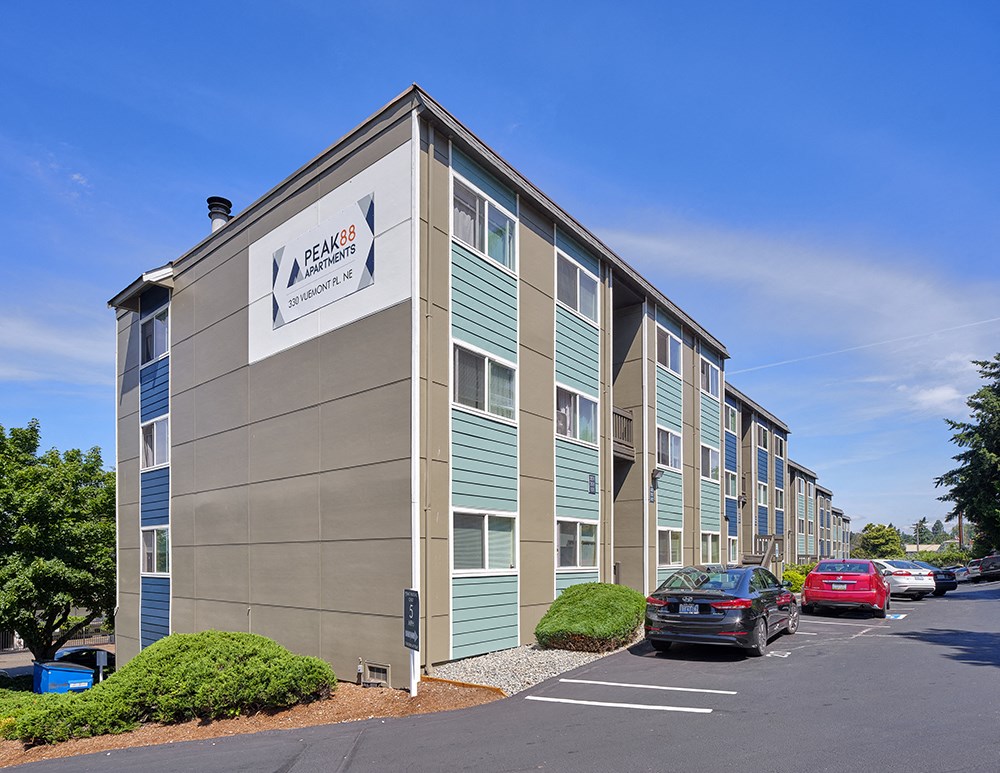 Building corner with parking below to the right. Bushes and landscaping.