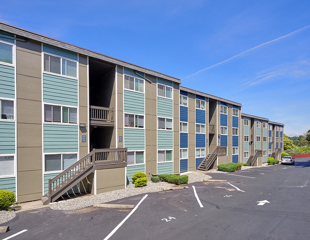Outside stairs lead to the apartment building with parking in front, landscaping, and mountains in the background.