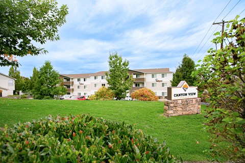 Grassy field and landscaping with Canyon View apartments and sign in the distance. at Canyon View, Idaho, 83501