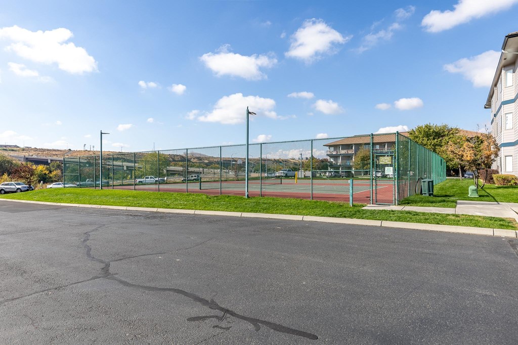 a tennis court in front of a building with a green fence  at Shoreline Village, Richland