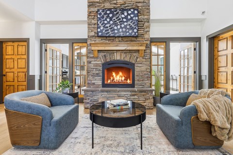 A living room with a stone fireplace and two blue chairs.