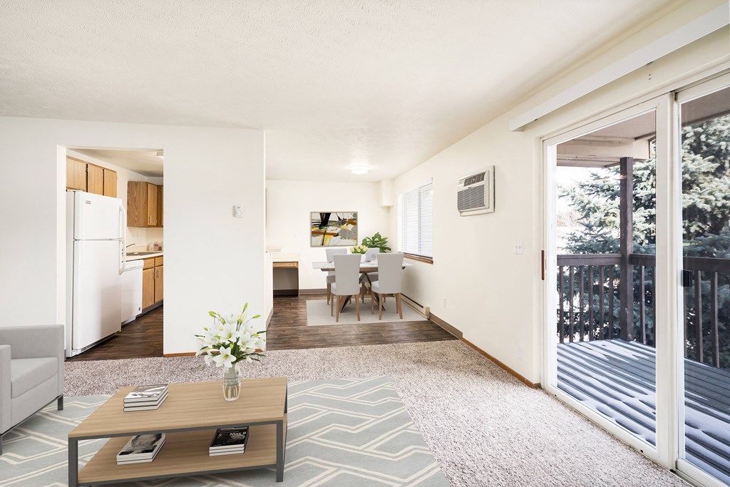 Living room with taupe carpet looking into dining room staged with a dining set. A private balcony is to the right with great natural light.at Clearwater, Post Falls, ID