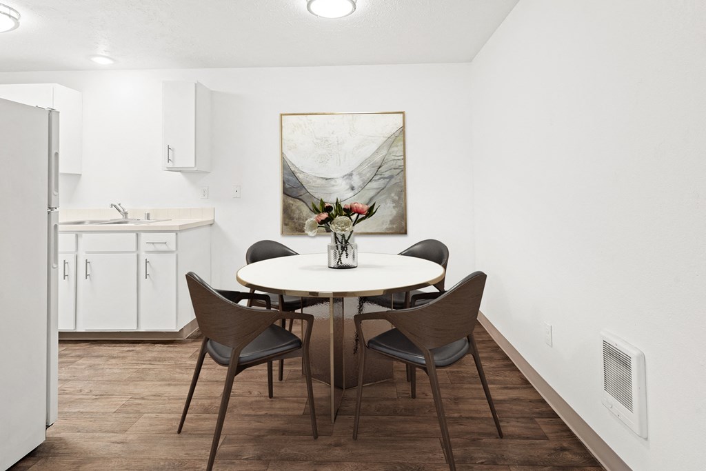 A dining area with hardwood floors and access to the kitchen. Staged with a round table, 4 chairs, and wall art.at North Pointe, Post Falls, ID 83854