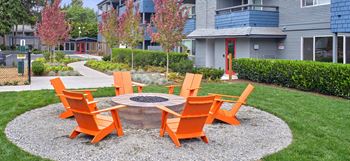 a fire pit surrounded by orange chairs in the middle of a grassy area