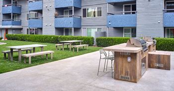 a picnic area with a grill and picnic tables in front of an apartment building
