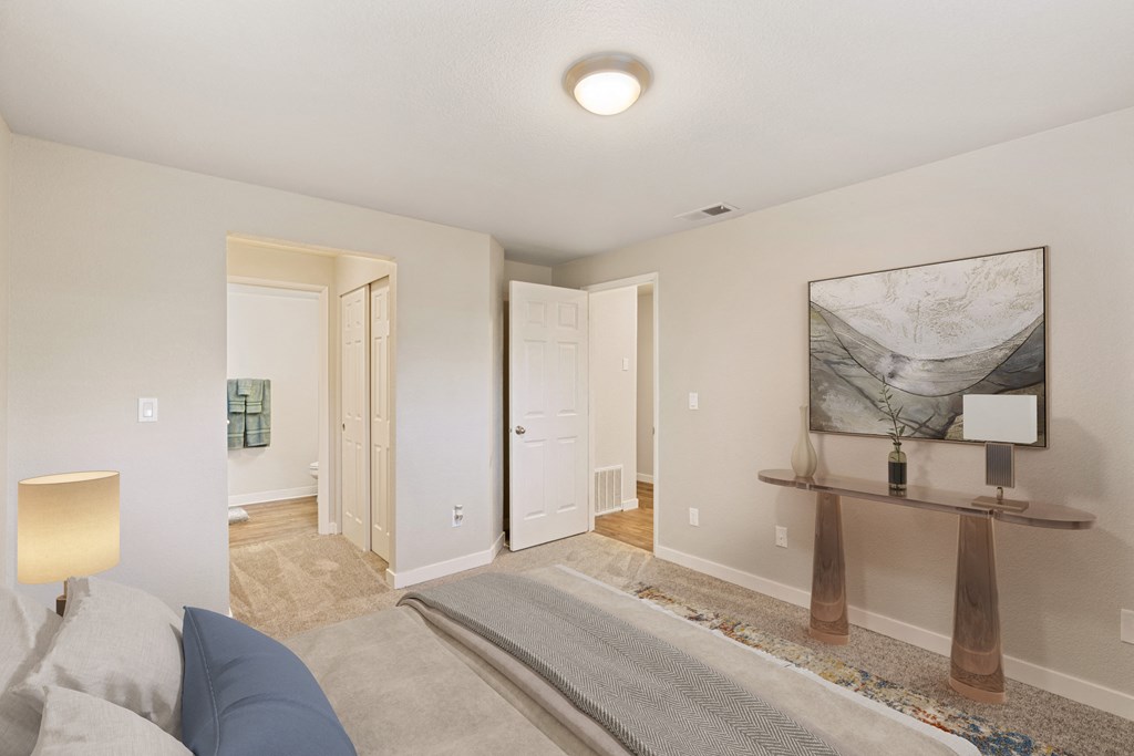 Bedroom with hallway door and door to en suite bathroom, staged bed, carpet, side tables and art on walls.at Capitol Crossing, Olympia