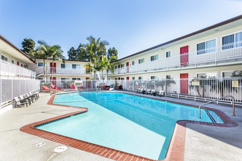 Outdoor swimming pool with sun chairs, a lounge area lined with apartments, and palm trees at Pacific Sands, San Diego, CA