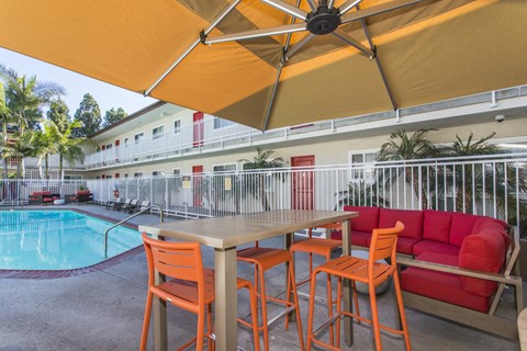Outdoor Lounge area with table, bar stools and couch. Swimming Pool is several feet away from the lounge at Pacific Sands, San Diego, 92117