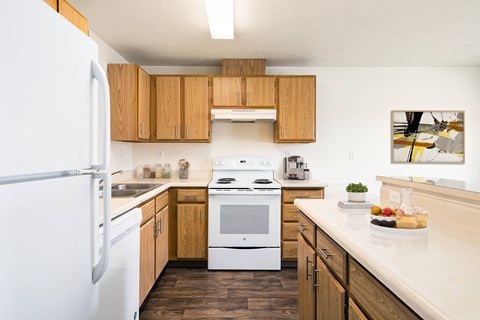 A kitchen with hardwood floors, top and bottom cabinet storage, and white appliances. Breakfast bar and island to the right.at Clearwater, Post Falls, 83854