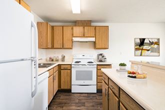 A kitchen with hardwood floors, top and bottom cabinet storage, and white appliances. Breakfast bar and island to the right.at Clearwater, Post Falls, 83854 - Photo Gallery 3