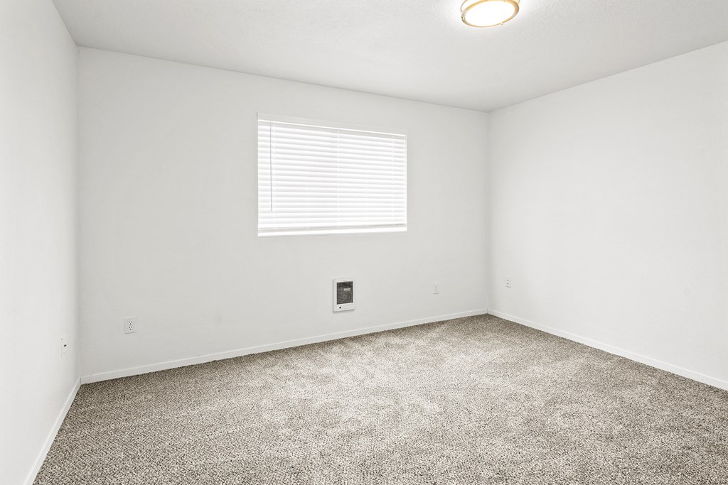 Bright empty bedroom with taupe carpet, white walls and white horizontal blinds on a window on the opposite wall.at North Pointe, Idaho, 83854