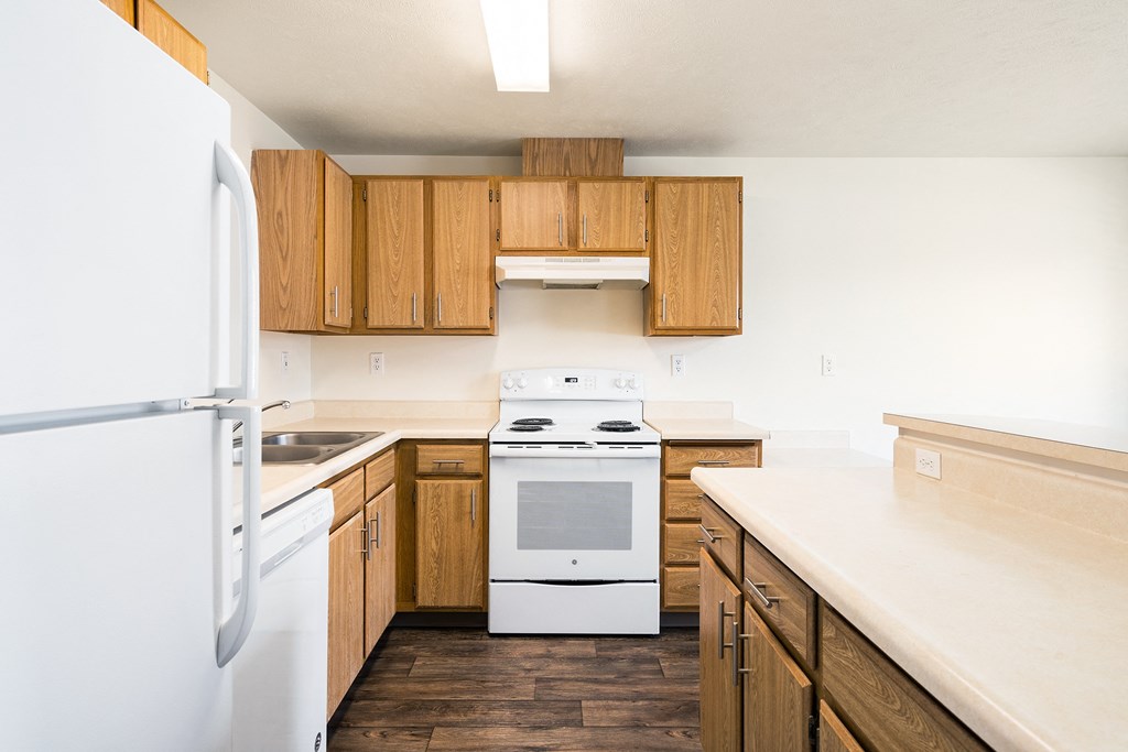 Apartment kitchen with hardwood floors, wood cabinets, spacious countertops, and white appliances.at Clearwater, Post Falls Idaho
