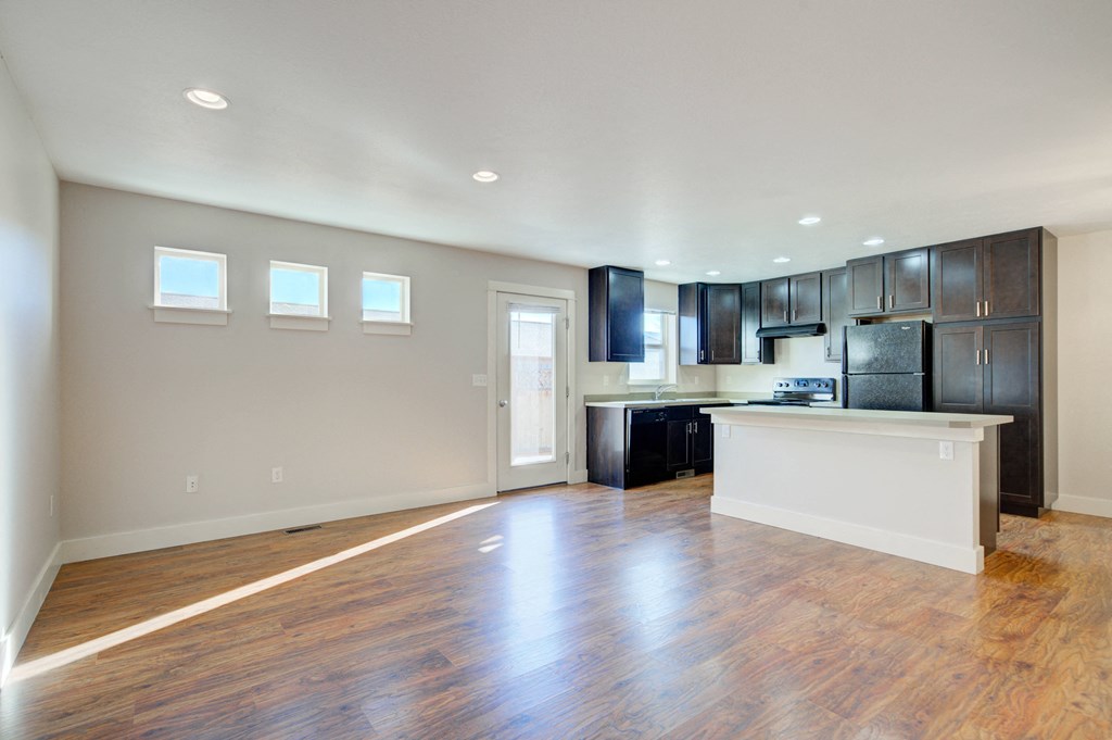 an empty living room and kitchen with wood flooring and black cabinets at Copper Pines, Bozeman, Montana