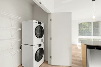 Large kitchen pantry with white metal shelves on left and full-size washer and dryer on right side. at The Duo Apartments in University Place.at The Duo, Washington, 98466