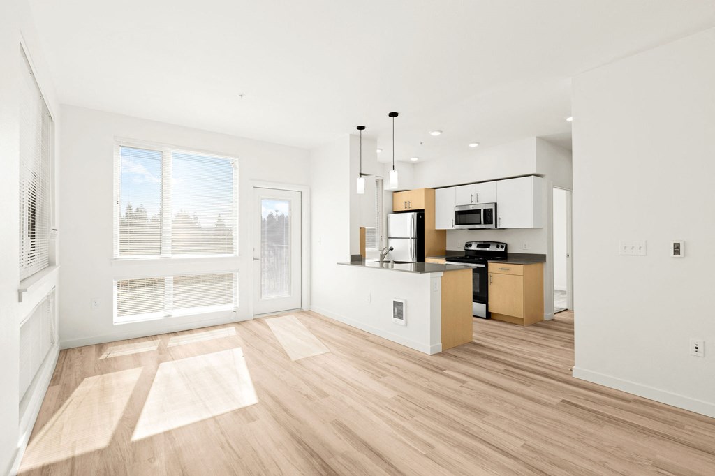an empty living room with a kitchen and a large window at The Duo, University Place Washington