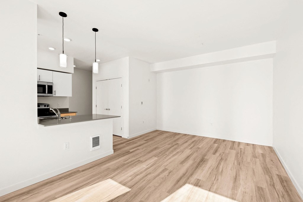 an empty living room and kitchen with white walls and wood flooring at The Duo, University Place