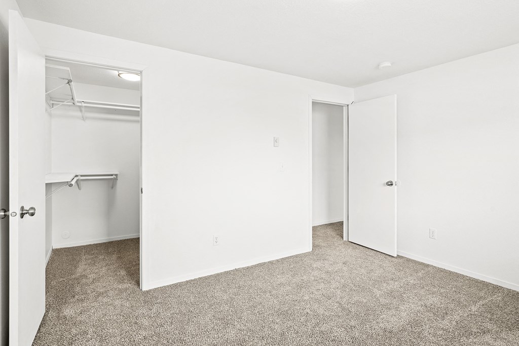 Bright white bedroom with taupe carpet and two open doors. One door leading to hallway, one door leads to walk-in closet with rods at multiple levels.at North Pointe, Idaho
