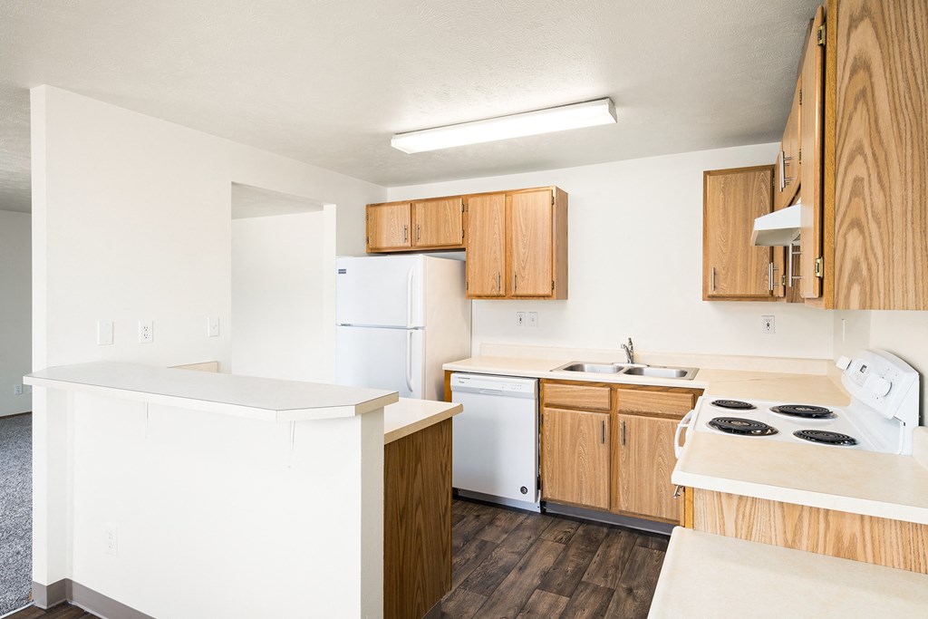 A kitchen with hardwood floors, a full fridge, dishwasher, double bowl sink, stovetop, oven, and breakfast bar. at Clearwater, Post Falls, 83854