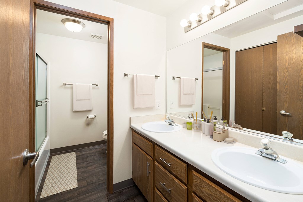 A full bathroom with a double vanity sink, a large mirror, cabinet storage, and a door to the toilet, shower, and bath.at Clearwater, Post Falls Idaho