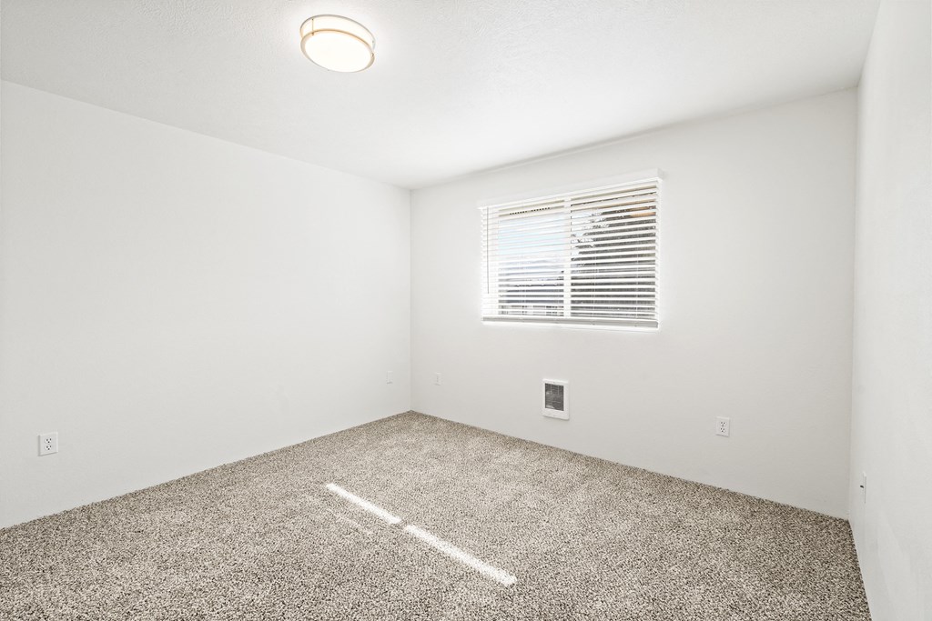 Bright empty bedroom with taupe carpet, white walls and white horizontal blinds on a window on the opposite wall.at North Pointe, Idaho, 83854