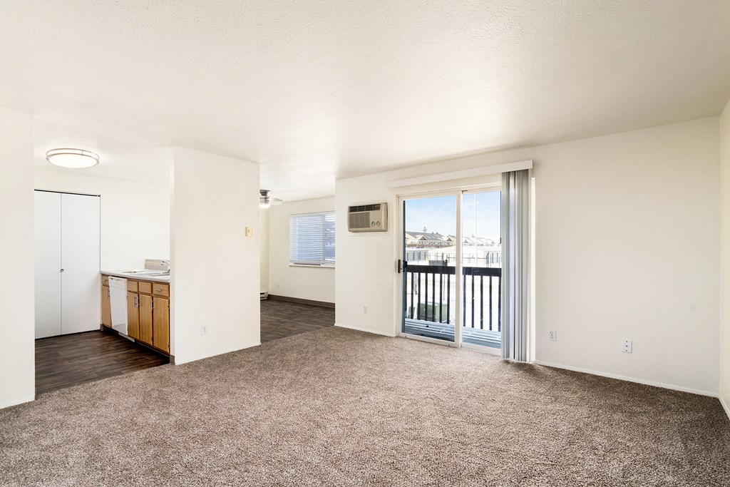 Light-filled living room with white walls, balcony access, and taupe carpets that meet the hardwood floors of the kitchen and dining room.at Clearwater, Post Falls, 83854