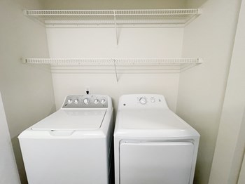 In-home top-loading washer and front-loading dryer with shelving storage above. - Photo Gallery 7