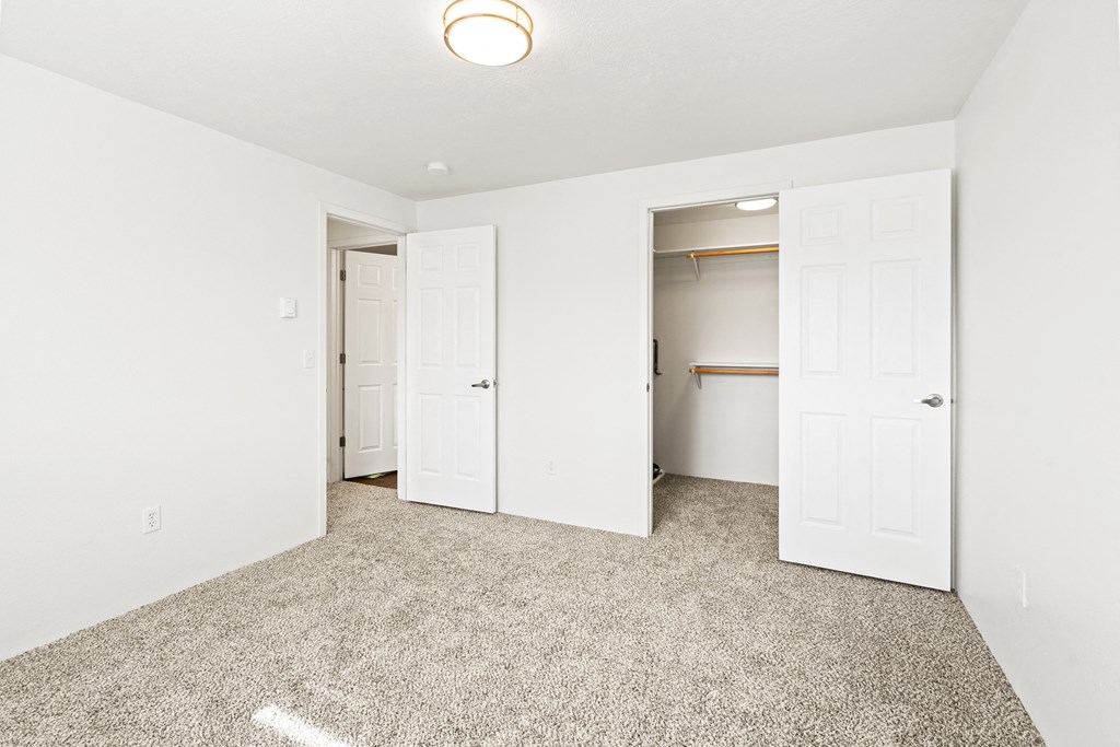 Bright white bedroom with taupe carpet and two open doors. One door leading to hallway, one door leads to walk-in closet with rods at multiple levels.at North Pointe, Post Falls Idaho