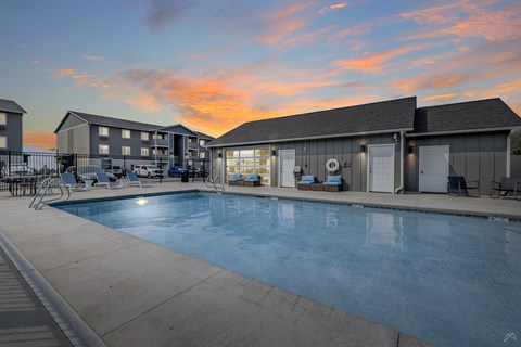 A swimming pool in front of a building with a sunset in the background.