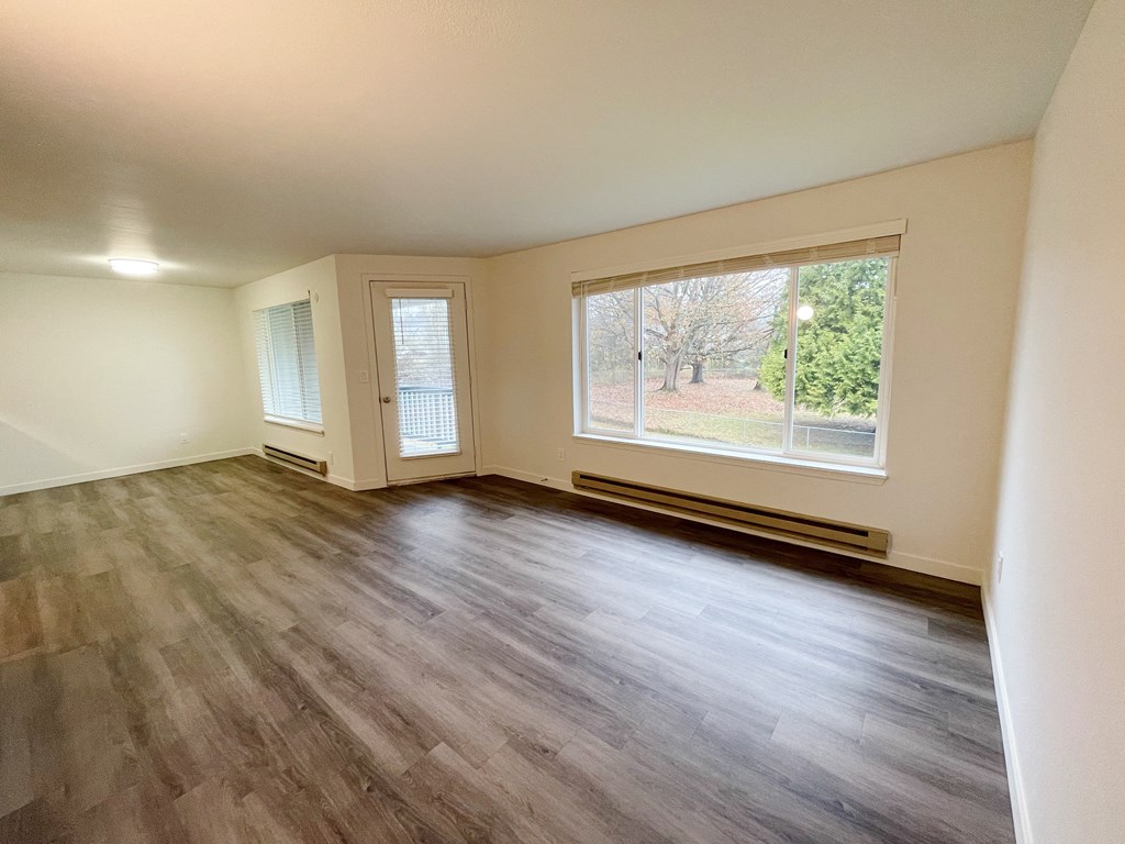 Spacious living room with wood-like flooring, an oversized window with nature views, and a door to a private balcony.at The Trail, Snohomish