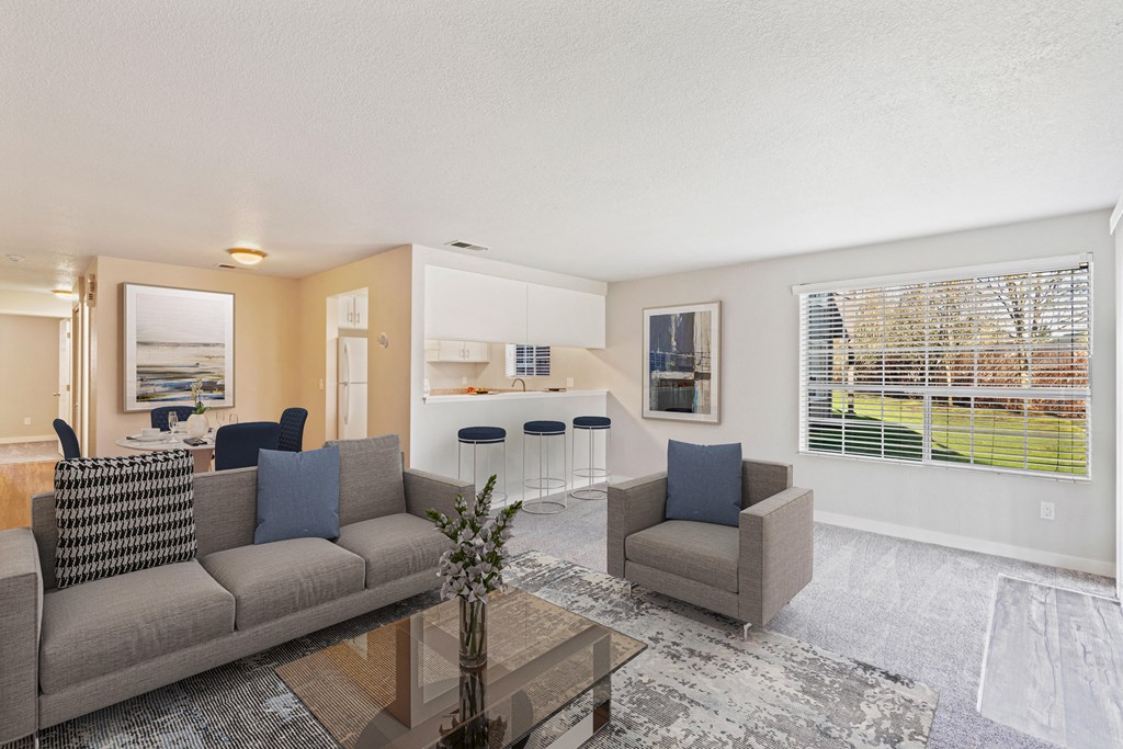 Carpeted living room with view of kitchen and pass-through bar with stools. A large window looks out on a grass lawn.at Capitol Crossing, Olympia, WA