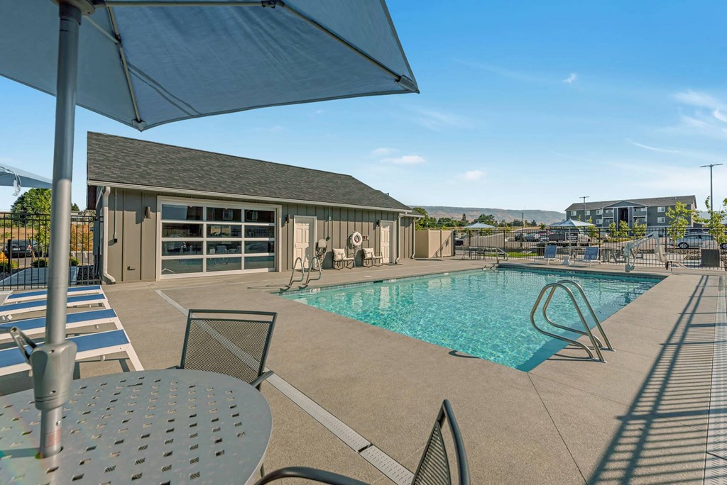 Bright blue pool with lounge chairs, umbrella-covered seating, and a view of the clubhouse. at Altitude, East Wenatchee, WA, 98802
