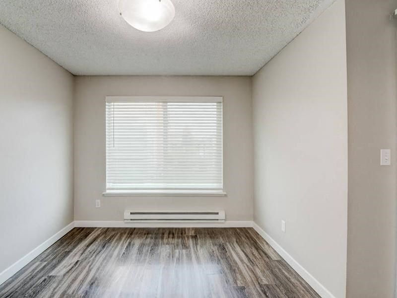 A dining room with taupe walls, wood-like flooring, a large window with blinds on the back wall, and overhead lighting. at Pointe East, Washington, 98424