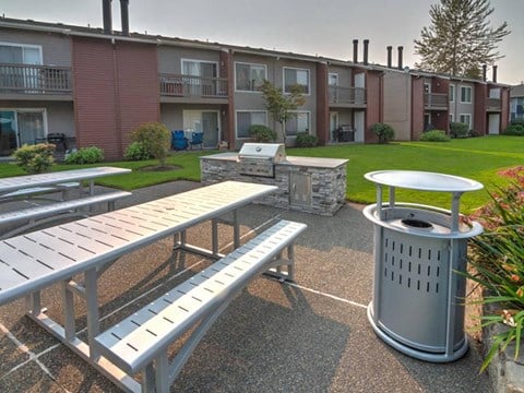BBQ and picnic area with two picnic tables, a stainless steel BBQ, and a large green lawn and landscaping behind. at Pointe East, Fife, WA, 98424