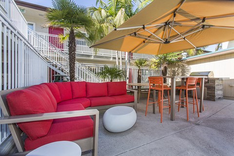 Outdoor resident lounge with a red patio sofa, high table with orange chairs next to the pool, with a gas BBQ at Pacific Sands, San Diego, California