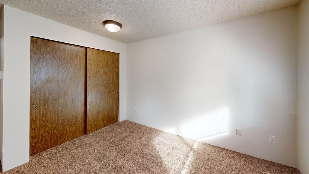 Comfortable bedroom at Heritage Grove Apartments in Renton WA with neutral walls, carpeted floor, and a window view to the outdoors.