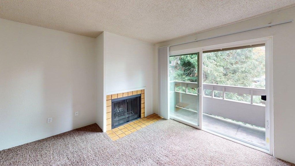Inviting living room at Heritage Grove Apartments Renton WA with fireplace, large window for natural light, and carpeted flooring.