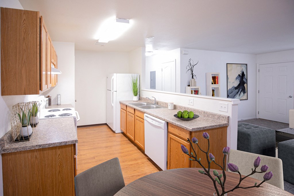 Bright open kitchen and living areas, with honey-colored cabinets and faux wood flooring in the kitchen, and a half wall between the kitchen and the living room.at Canyon View, Idaho, 83501