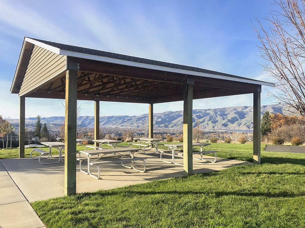 Outdoor community pavilion with many benches surrounded by grass and overlooking the Snake River mountain range.at Canyon View, Lewiston Idaho.
