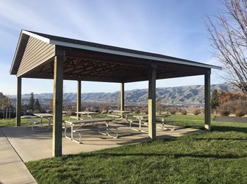 Outdoor community pavilion with many benches surrounded by grass and overlooking the Snake River mountain range. - Photo Gallery 3