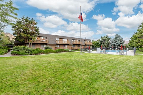 A grassy area in front of a building with an American flag on a pole.