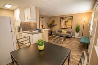 Dining area flows into kitchen and living room. Staged with dining set, couch, table, and plants. - Photo Gallery 2