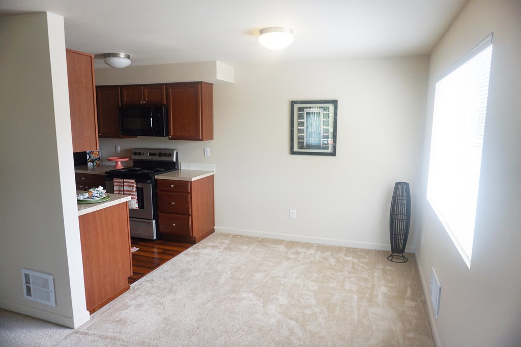 a kitchen and dining area with a carpeted floor and large window at Heritage Grove Apartments in Renton, WA