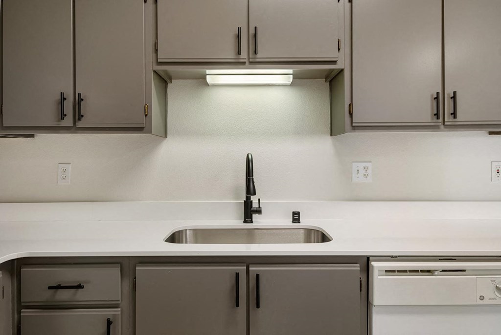 A kitchen with white countertops, a stainless steel sink, gray cabinets and a dishwasher.at Shoreline Village, Richland