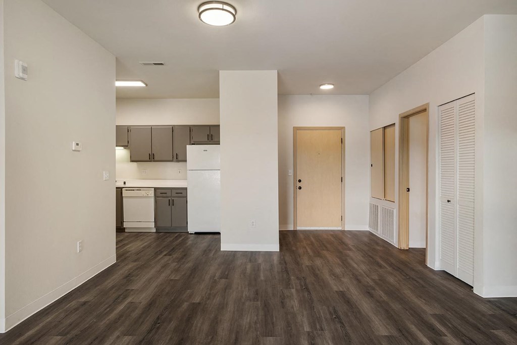 a living room with wood-style flooring, white walls and a kitchen in the background.at Shoreline Village, Washington, 99352
