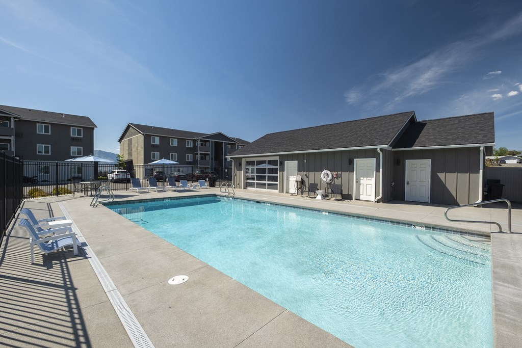 a swimming pool with lounge chairs and umbrellas in front of a building  at Altitude, East Wenatchee