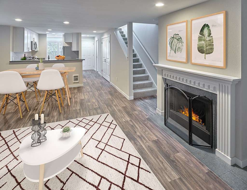 Living room with a gas fireplace, mantle, wood-like floors opens into dining room with stairs to the right next to a hallway.at Edmonds Gateway, Edmonds, WA 98026