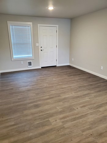 Apartment entryway, vinyl window with closed blinds to the left of the front door, wood-like flooring, and wall outlets. - Photo Gallery 10