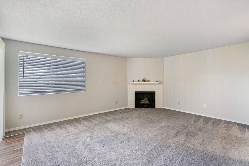 Spacious living room with gray carpet, fireplace, and mantle in the center, and an entrance to outside on the left. at Capitol Crossing, Olympia, WA 98501