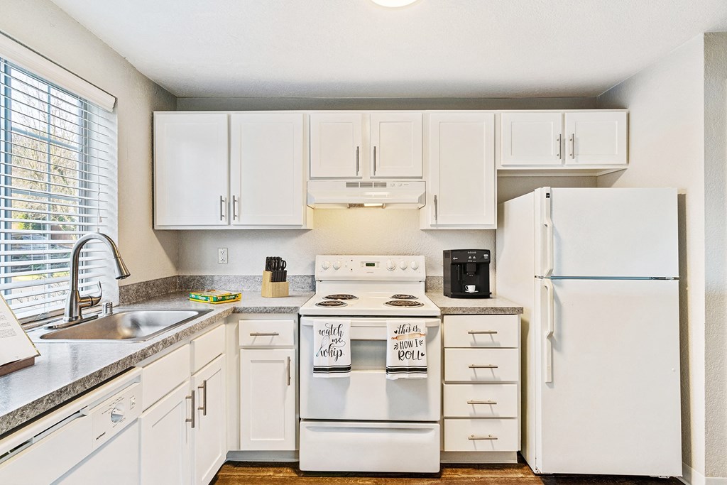 Kitchen L-shaped kitchen with white cabinets, a large window above the sink, and a white dishwasher, oven, stovetop, full-size fridge.at Capitol Crossing, Olympia, WA