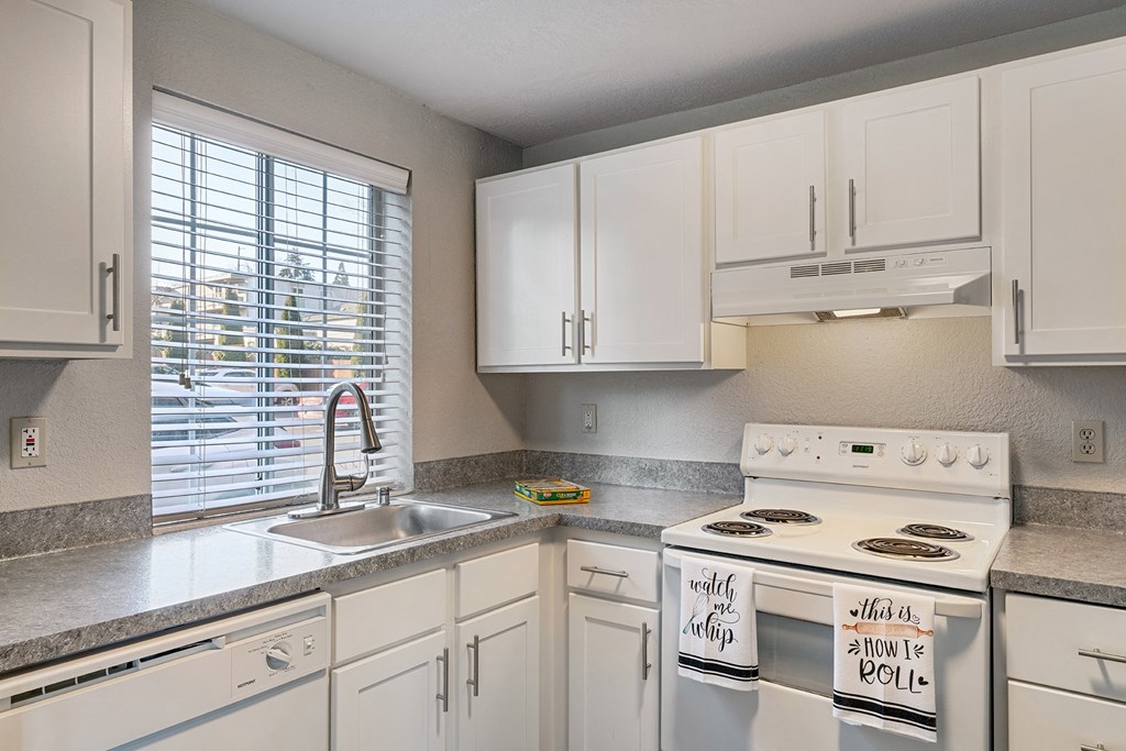 Kitchen with white cabinets, a window above the sink, and a white stove top and oven with staged hand towels.at Capitol Crossing, Olympia, Washington